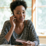 Woman with Short Natural Hair on a Phone Call, Holding a Credit Card at a Bright Kitchen Table.