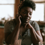 unitedhealthcare-therapist-philadelphia-pa - Caring Clarity Counseling Woman in a Black-and-white Striped Shirt Talks on a Cell Phone, Resting Her Chin on Her Hands with a Thoughtful Expression Indoors at Home.