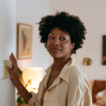 Woman with Natural Hair Stands in a Doorway, Hand Resting on a Light Switch in a Cozy Living Space.