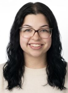 Smiling Woman with Long Dark Hair and Pink Glasses, Wearing a Beige Sweaters in a Head-and-shoulders Portrait.