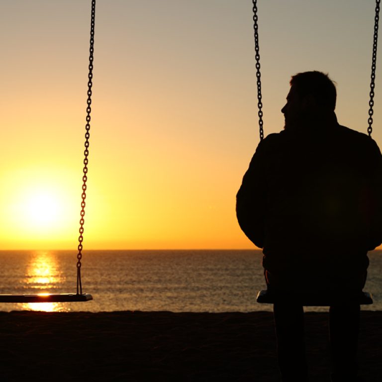 Man alone on a swing looking at empty seat